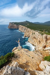 Tourist stretches her arms in the air, view of steep cliffs by the sea, coastal landscape, cliffs
