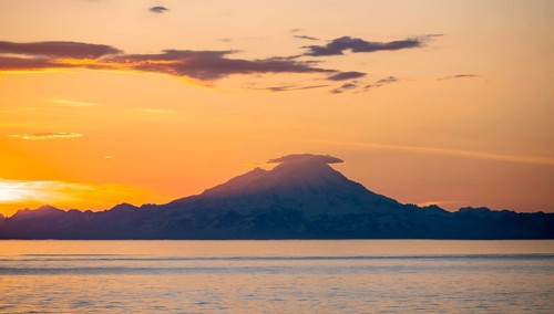View of Cook Inlet on white mountain peaks of Mount Redoubt at sunset, picturesque golden light of