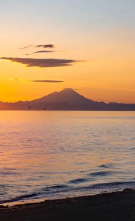 View of Cook Inlet on white mountain peaks of Mount Redoubt at sunset, picturesque golden light of