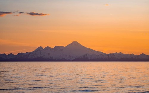 View of Cook Inlet on white mountain peaks of Mount Iliamna at sunset, picturesque golden light of