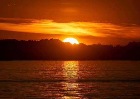 Sun sets behind mountain peaks, view of Cook Inlet at sunset, picturesque golden light of the