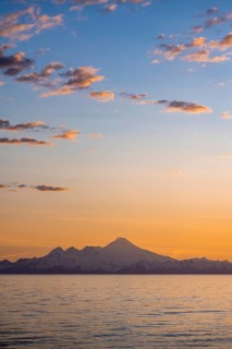 View of Cook Inlet on white mountain peaks of Mount Iliamna at sunset, picturesque golden light of