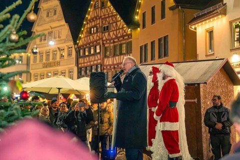 A man gives a speech next to Santa Claus on a market square with half-timbered houses, Christmas