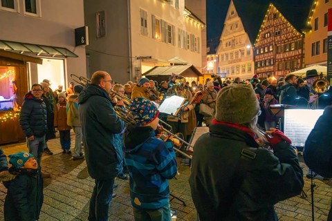 A brass band plays on a busy street surrounded by bright decorations, Christmas market 2025,
