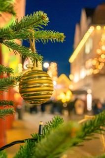 Golden Christmas ball on a pine branch surrounded by blurred lights, Christmas market 2025, Nagold,