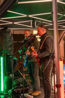 Two musicians on a stage at night playing guitars surrounded by festive lighting, Christmas market