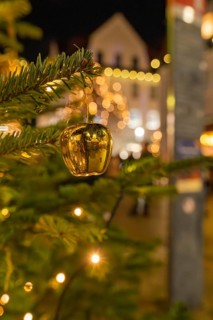 Close-up of a golden Christmas ornament on a pine branch with lights in the background, Christmas