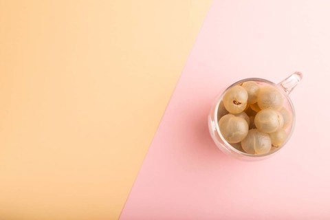 Ripe peeled Longan in glass on pink and orange pastel paper background, top view, flat lay, copy