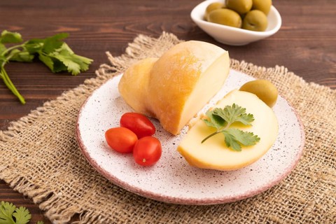 Smoked Mozzarella cheese, with tomatoes and olives on brown wooden background and linen textile,