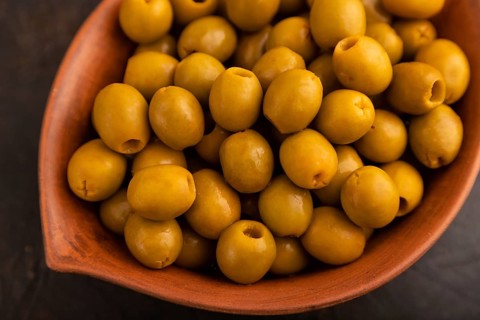 Fresh green olives in ceramic clay bowl on black concrete background. top view, close up, selective