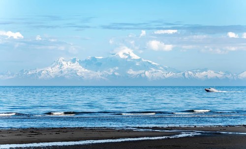 View over Cook Inlet to white mountain peaks of Mount Iliamna, motor boat rides on the ocean,