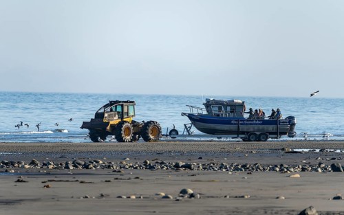 Motor boat on a boat trailer is driven into water by a tractor on a beach, Anchor Point, Alaska,