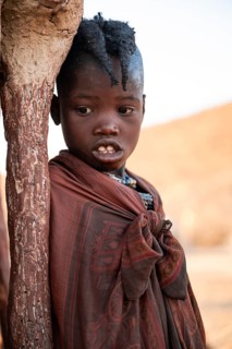 Himba girl leaning at a traditional clay hut, in the morning, traditional Himba village, Kaokoveld,