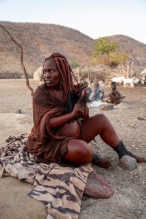 Married Himba woman sitting in front of the hut in the morning, traditional Himba village,