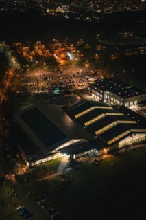 Aerial view of an illuminated building structure at night with surrounding parking spaces,