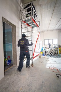 Worker on a construction site next to scaffolding, various construction works in the room,