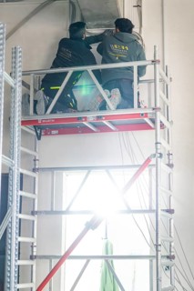 Two workers standing on scaffolding and working on a ceiling with strong light, electrician, new