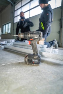 A drill is in the foreground while two workers work in the background, electrician, Neubau, Germany