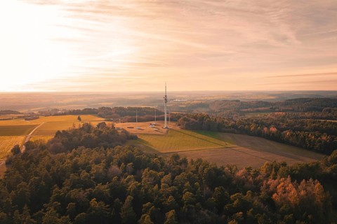 A radio tower rises in a vast landscape with forests and fields at sunset, Gechingen, Hecken and
