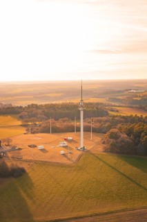 A radio tower stands in the middle of a large field, surrounded by forests at sunset, Gechingen,