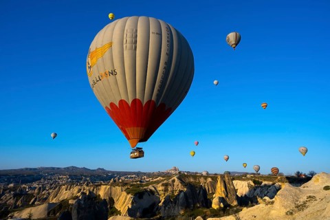 Large hot air balloon soars over a vast, rocky landscape under clear skies, Göreme National Park,