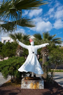 A white sculpture of a dancing man surrounded by palm trees under a clear sky, the swirling