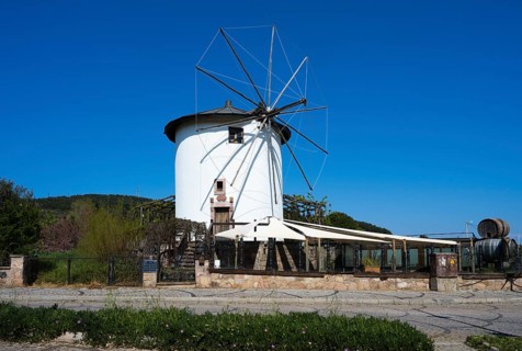A white windmill with wings in a quiet rural setting under clear skies, Cunda Windmill, Alibey