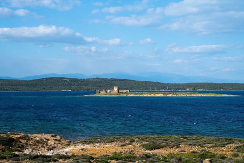 A small island with ruins is surrounded by a deep blue sea under clear skies, ruins of Agios Yorgis