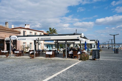 Seaside restaurant with outdoor seating area under blue and white skies, relaxed atmosphere and