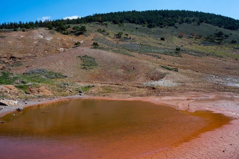 Small red lake in a geological mountain landscape under blue sky, geothermal area, rainbow rocks