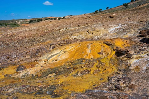 Area with yellow and brown rock formations under blue sky, geothermal area, rainbow rocks Tuzla,