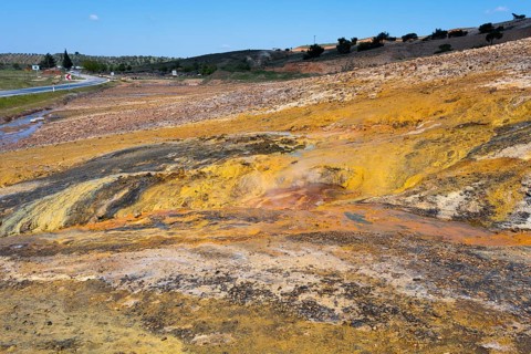 A colorful natural landscape with yellow and orange rocks next to a road under a blue sky,