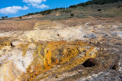 Geological landscape with hills and earthy tones under a partly cloudy blue sky, geothermal area,