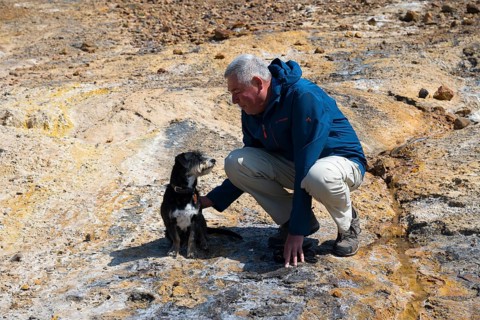 Man playing with dog in a rocky, natural environment, dressed in outdoor clothing, dog and man