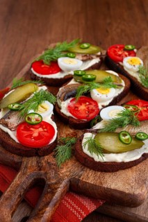 Sandwiches on rye bread with sprats, quail eggs, fresh tomatoes and pickled cucumber, on a wooden