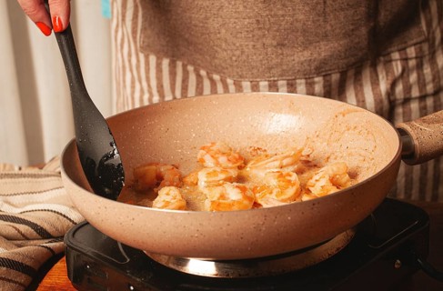 A person is stirring shrimp in a frying pan on the stovetop. The kitchen is warm and inviting, with