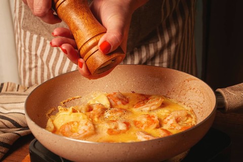 A person is cooking a shrimp omelette in a warm kitchen. Shrimp and eggs mix in a skillet as they
