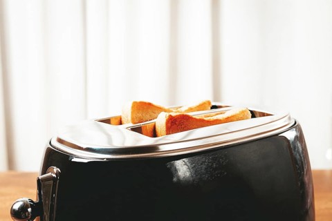 Two slices of bread are toasting in a shiny metal toaster, set on a countertop in a warm kitchen.
