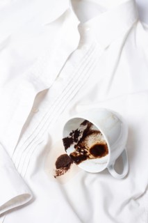 A white cup with the remains of coffee, spilled, lies on a white shirt, there are no people, a soft