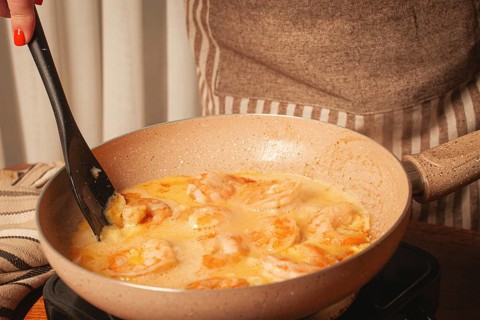 In a cozy kitchen, a person is stirring shrimp in a creamy sauce on the stove. The scene captures