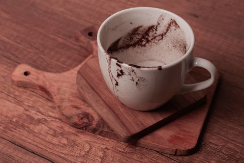 A white cup rests on a wooden cutting board showing remnants of coffee. The cozy setting suggests a