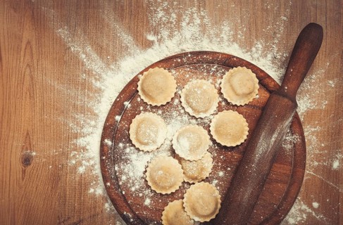 Fresh raw, uncooked ravioli, on a cutting board, with a rolling pin for dough, wooden background,