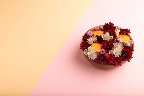 Wooden bowl with carrot slices and red Chrysanthemum flowers, Astrantia flowers, flower salad on