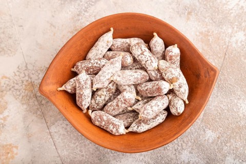 Small smoked Chicken sausages in clay bowl on brown concrete background. top view, close up