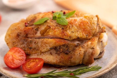 Fried Turkey Thigh with spices and rosemary on plate on brown concrete background and orange linen