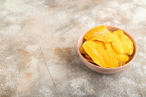 Dried Mango in ceramic bowl on brown concrete background. Side view, copy space. healthy food,