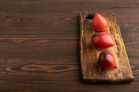 Red Heart shape tomatoes on cutting board on brown wooden background. Side view, copy space.