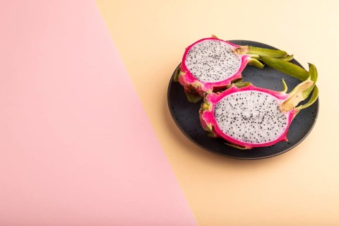 Ripe Pitaya on blue plate on pink and orange pastel paper background, side view, copy space,