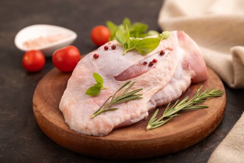 Raw Turkey Thigh with spices and rosemary on cutting board on black concrete background and linen