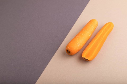 Orange Carrot on beige and gray pastel paper background. Side view, copy space, flat lay. healthy